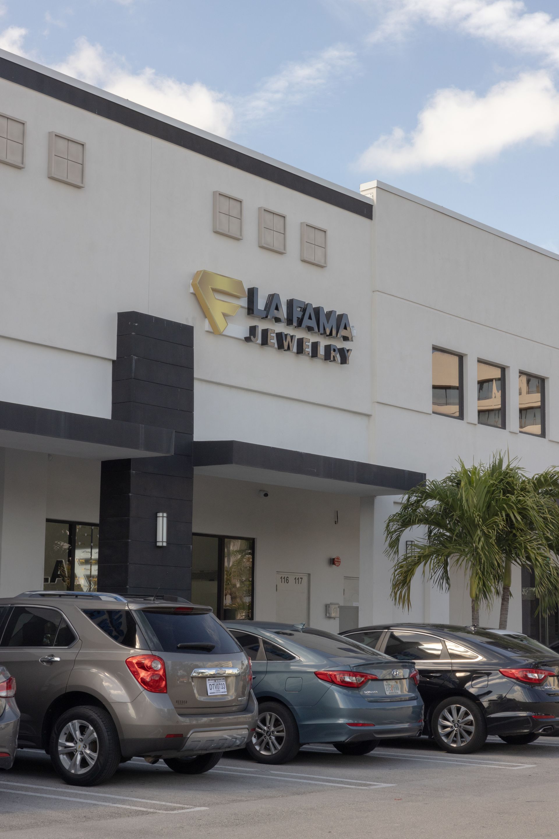 Una fila de coches están aparcados delante de un gran edificio blanco.