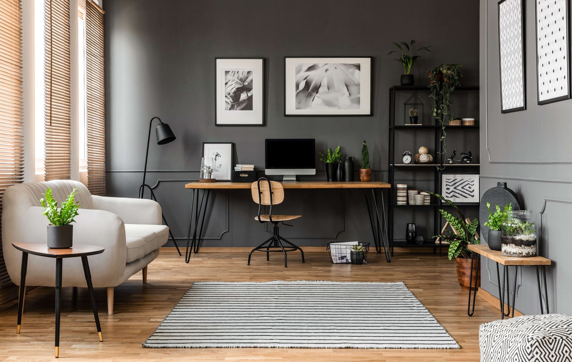 A modern office with a grey desk, chair, and shelving unit against dark walls, featuring a sofa and patterned area rug.