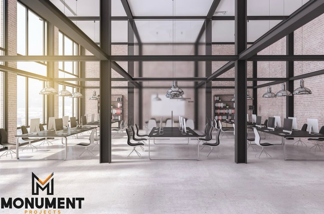 A modern, open-plan office space featuring industrial-style steel beams, brick walls, and rows of sleek desks.