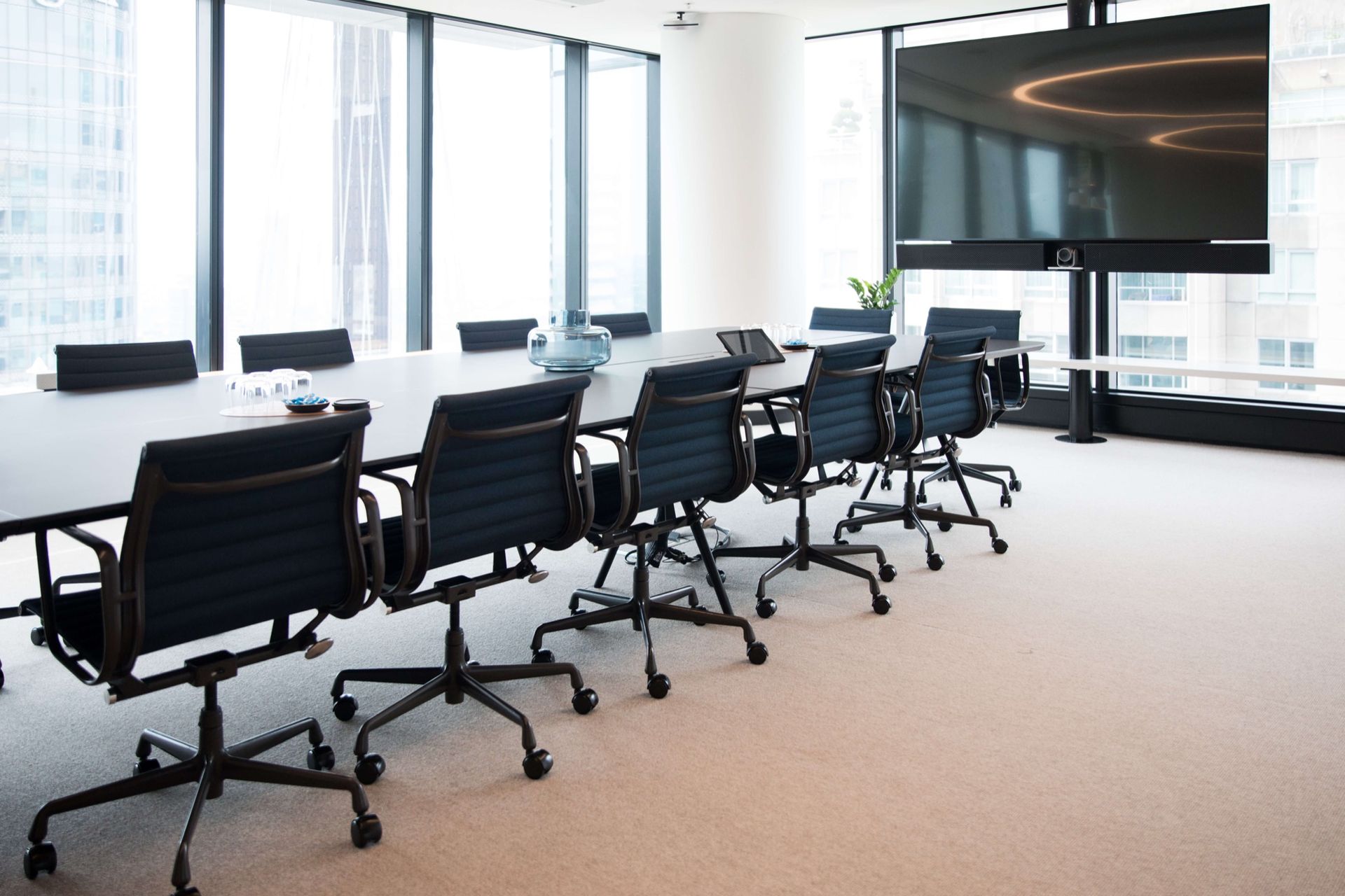A Modern, Brightly Lit Conference Room with A Long Table, Ergonomic Black Chairs, and A Wall-Mounted Display Screen.