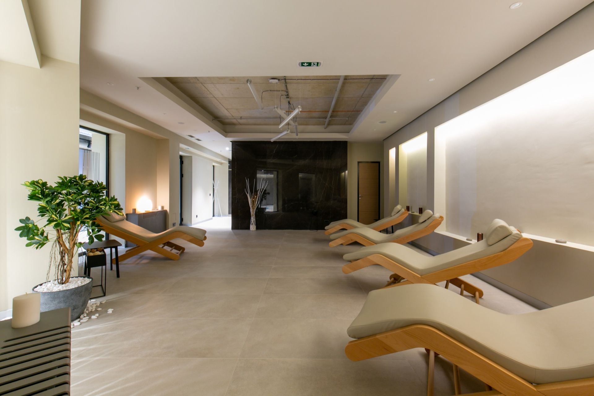 A tranquil spa relaxation room with several wooden lounge chairs, a potted plant, and soft, recessed lighting.