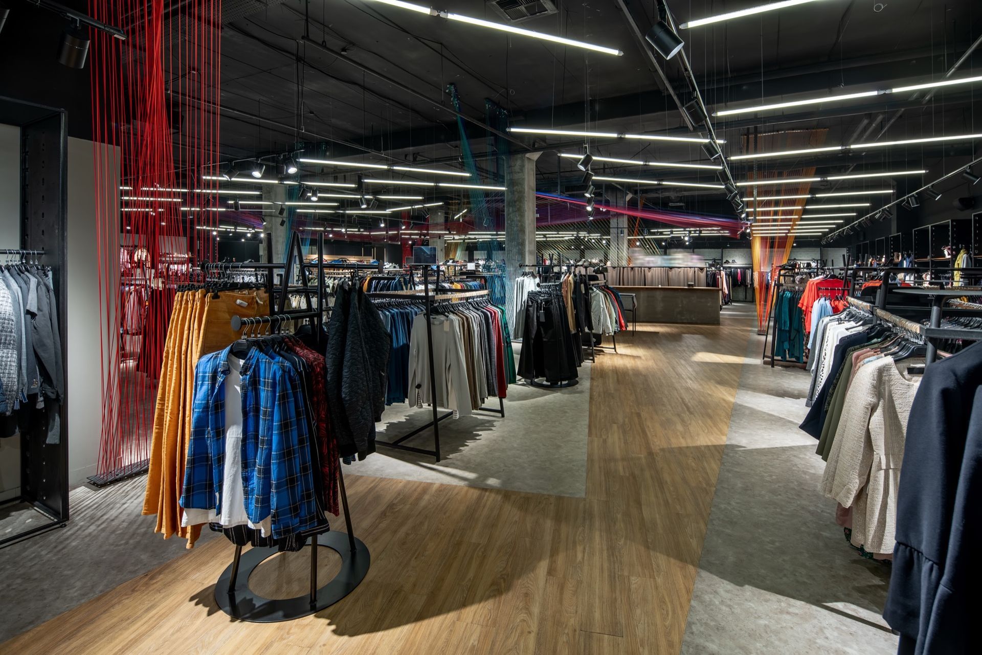 An interior view of a modern clothing store featuring racks of various garments, hardwood flooring, and industrial lighting.