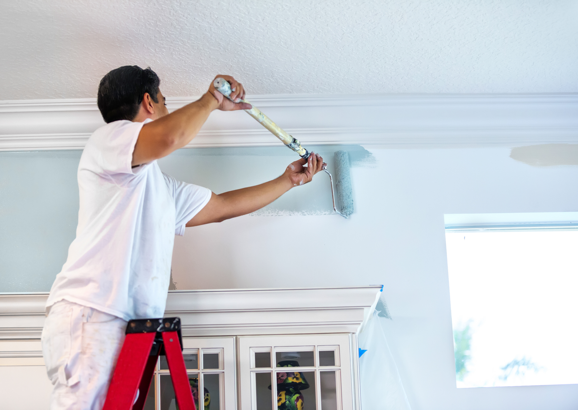 A man is standing on a ladder painting a wall.
