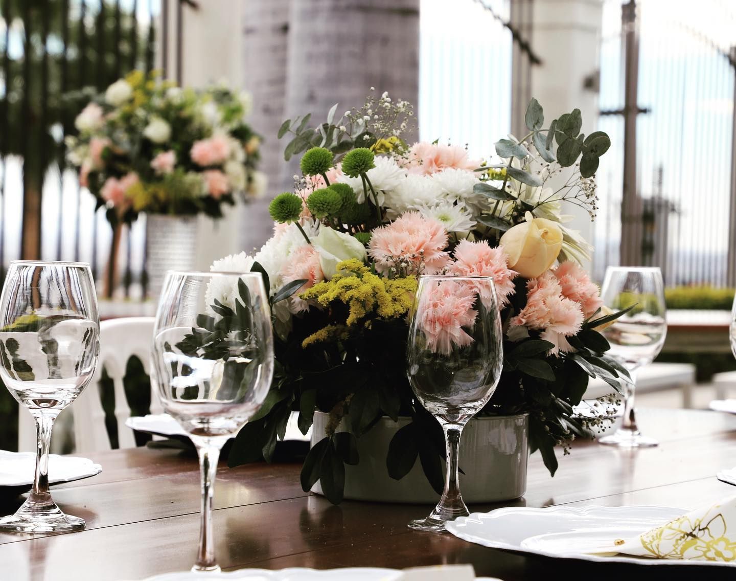 Una mesa con un jarrón de flores y copas de vino encima.