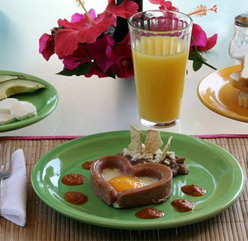 Un postre en forma de corazón en un plato verde junto a un vaso de jugo de naranja.