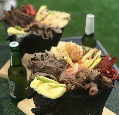 Sobre una mesa hay dos cuencos de comida junto a botellas de cerveza.