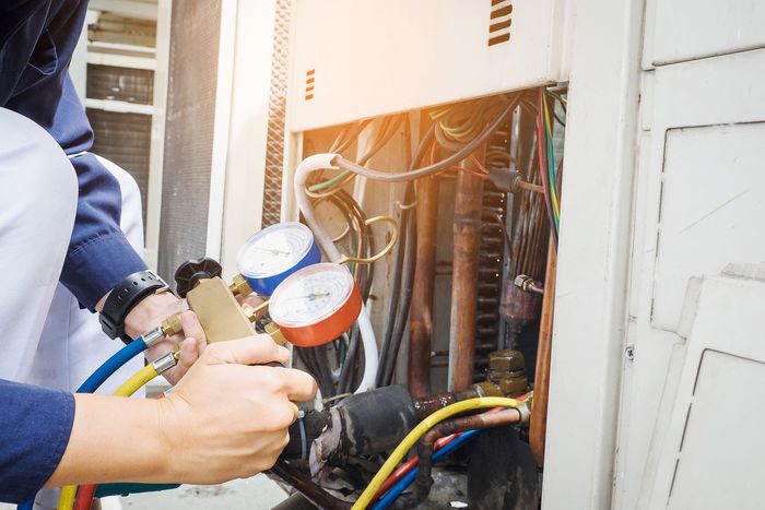 A man is working on an air conditioner outside of a building.