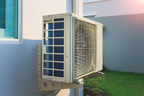 An air conditioner is mounted on the side of a building next to a window.