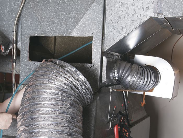 A person is working on a duct with a hose attached to it