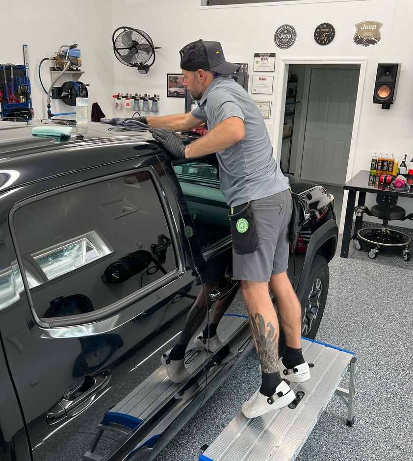 A man is standing on a ladder next to a black truck.