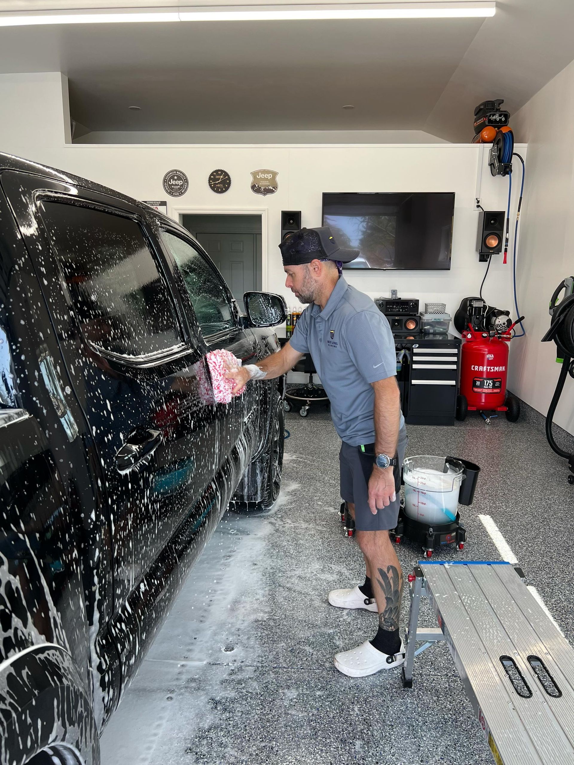 A man is washing a black truck in a garage.