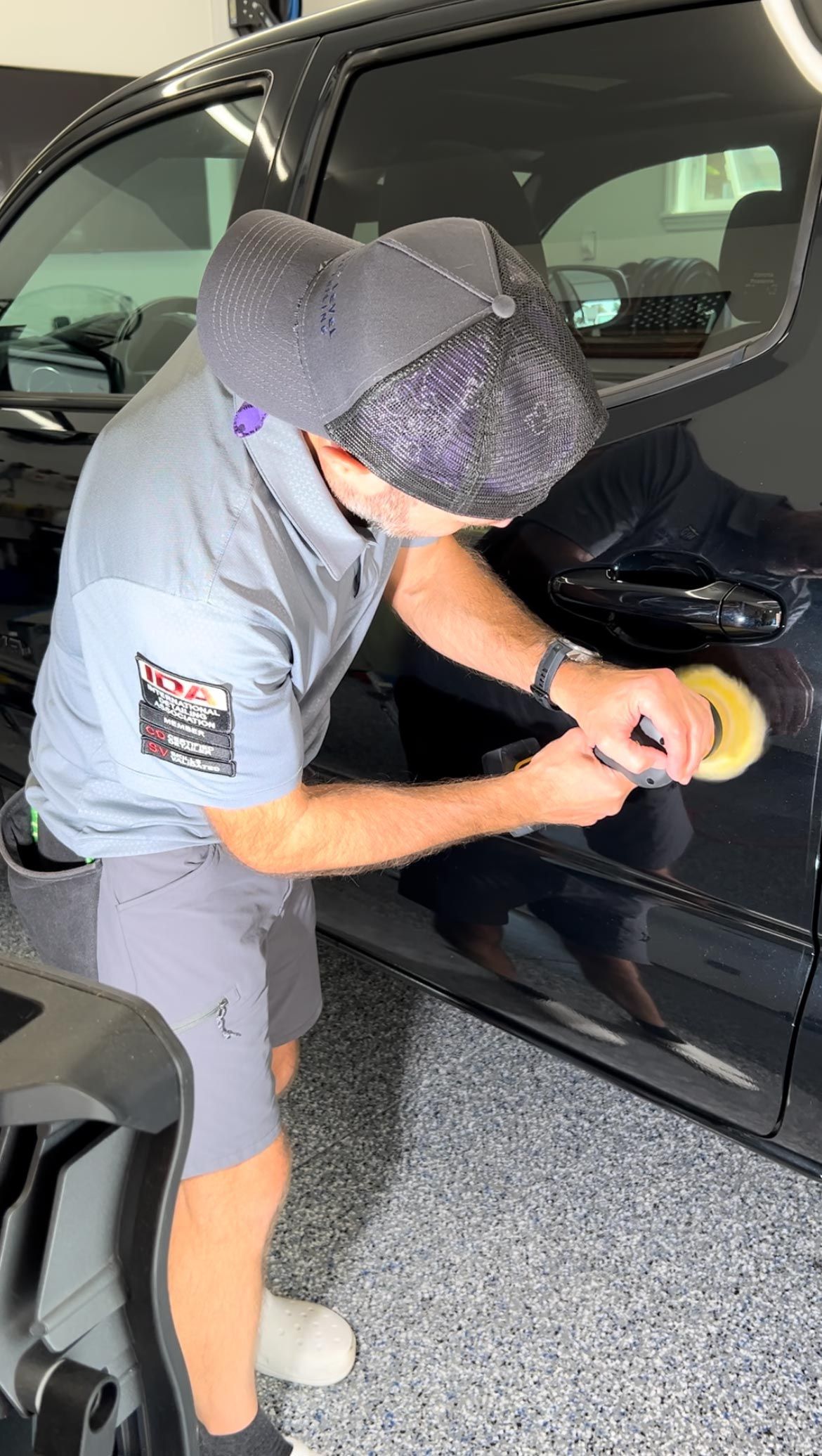 A man is polishing a black car in a garage.