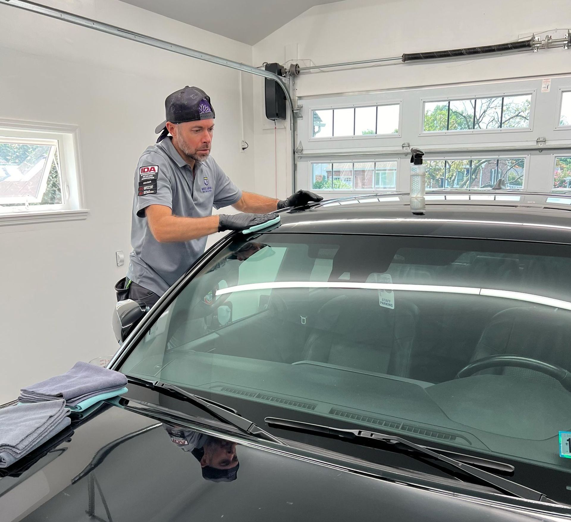 A man is cleaning the windshield of a black car in a garage.