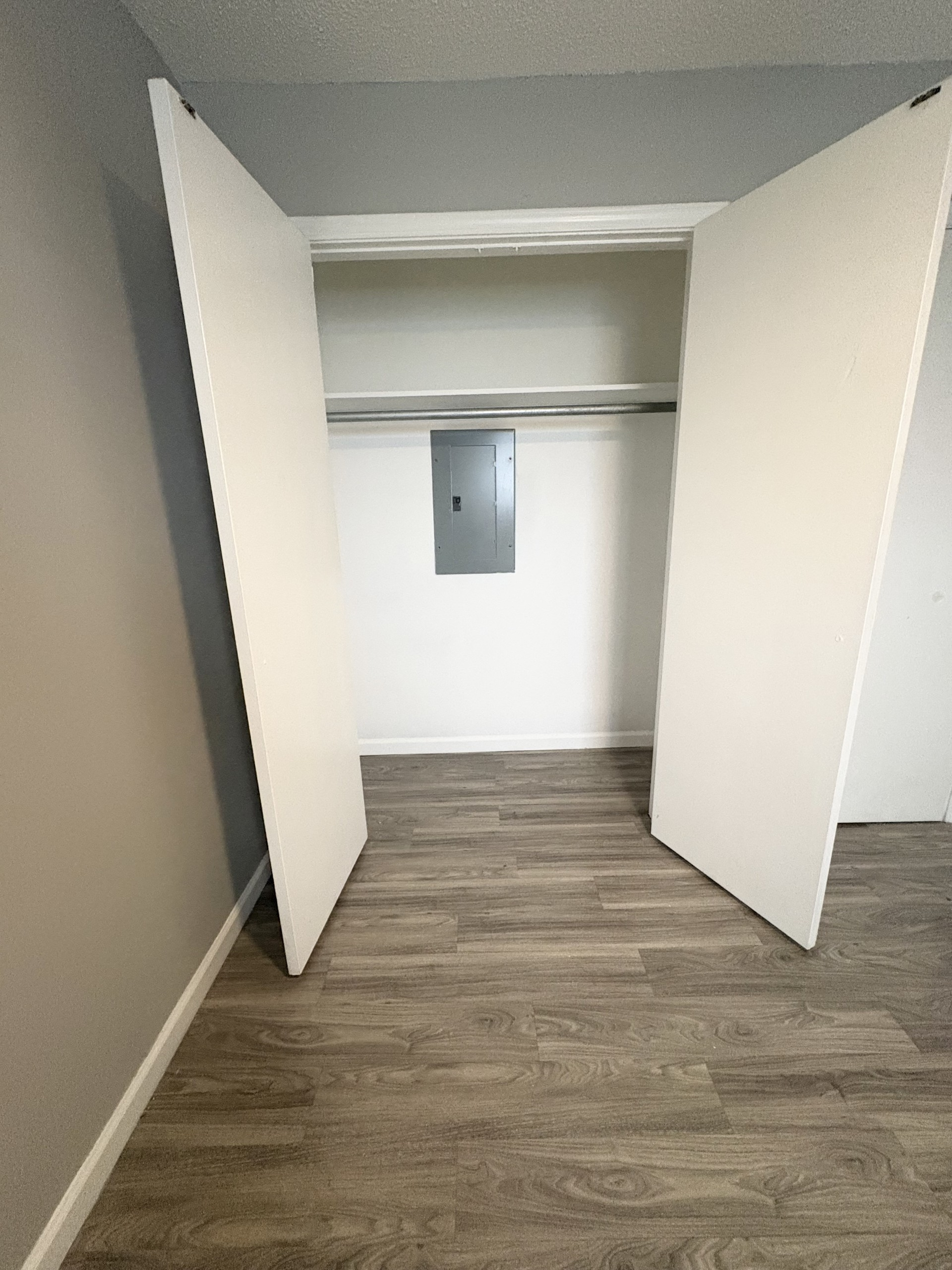 Open closet with white doors and wood-look flooring in a small room.