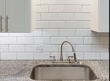 Kitchen sink with chrome faucet and white subway tile backsplash under light cabinets