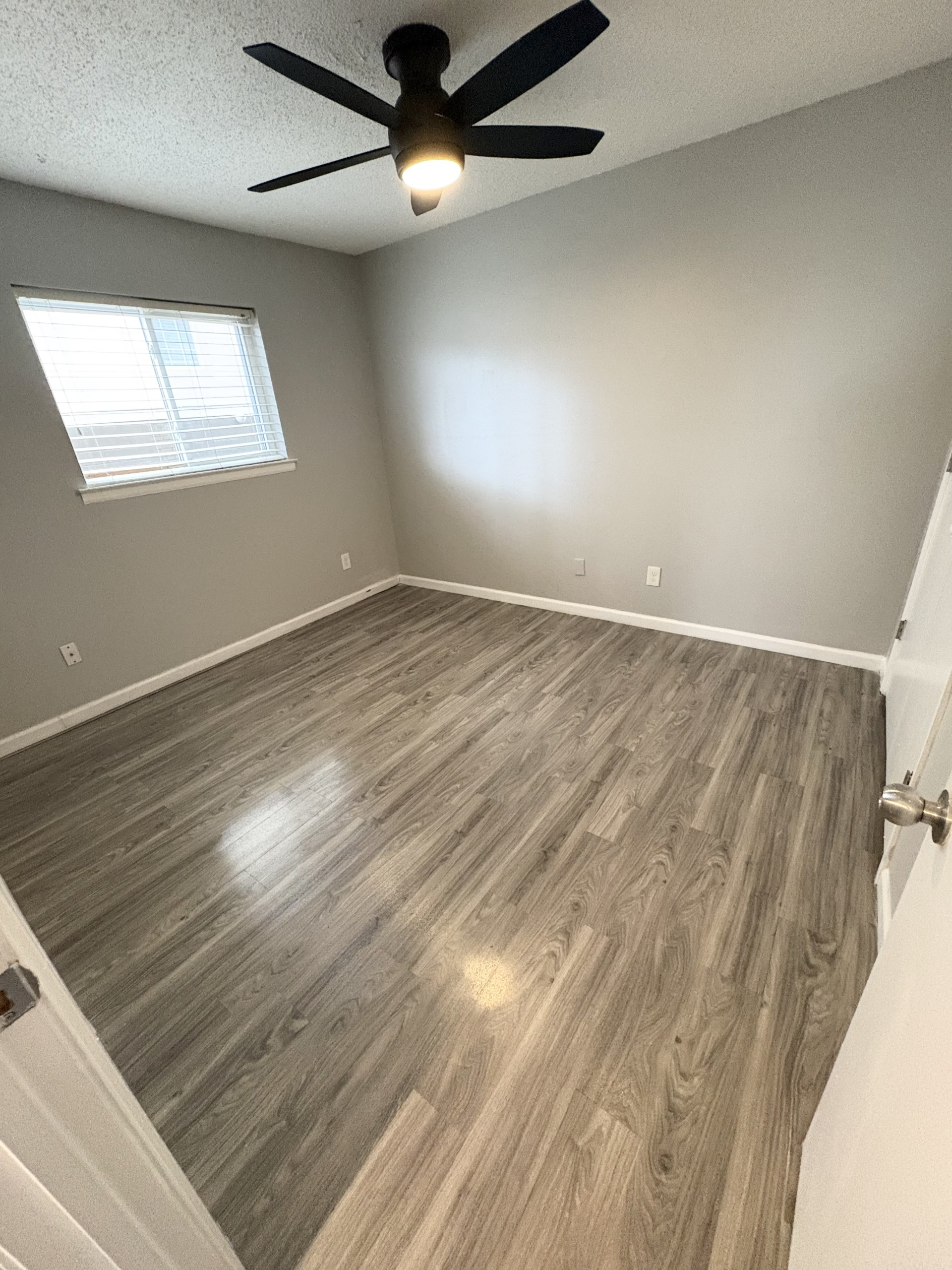 Empty bedroom with gray walls, wood-look flooring, a ceiling fan, and a window with blinds.