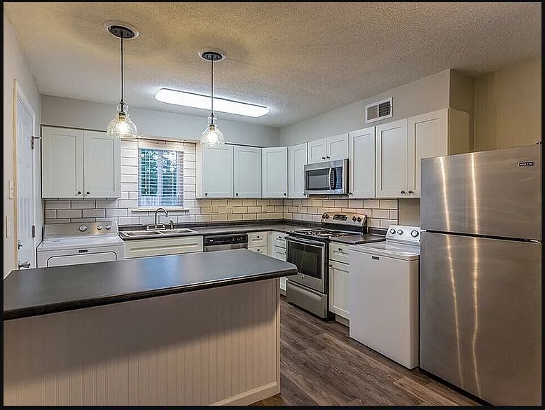 Bright modern kitchen with white cabinets, dark countertops, stainless appliances, and pendant lights