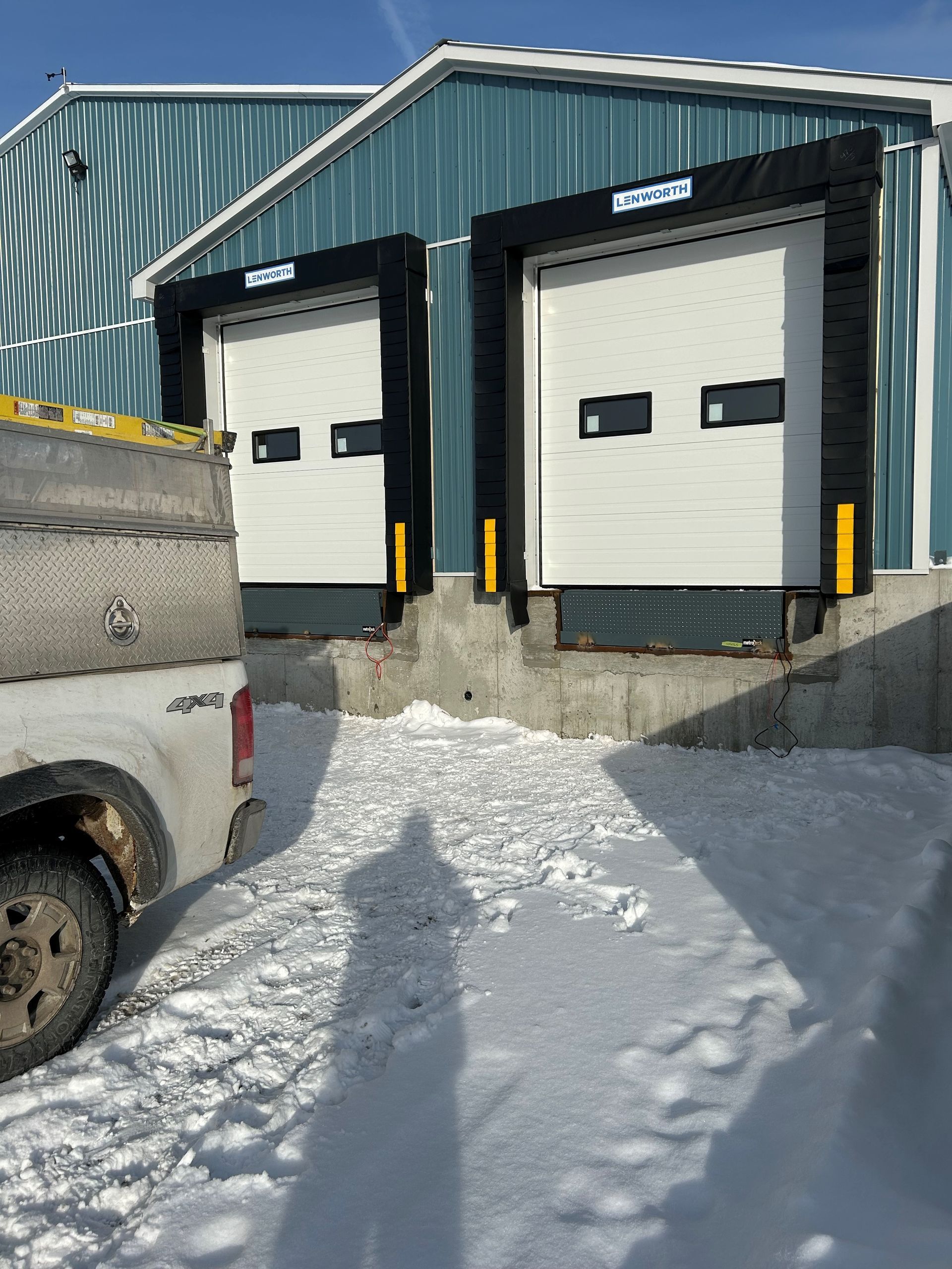 A truck is parked in front of a building with loading docks in the snow.