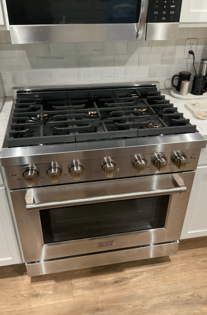 Stainless steel range with gas stovetop and oven, in a kitchen with white cabinets.