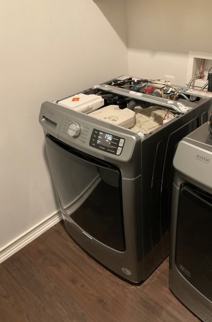 Open top silver dryer in a laundry room, revealing internal components and controls.