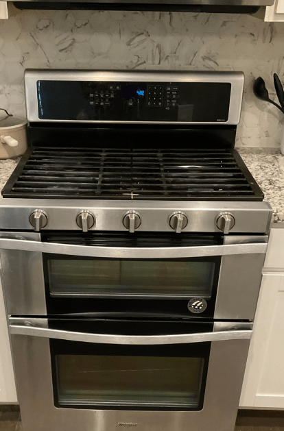 Stainless steel gas range with two ovens and black cooktop.