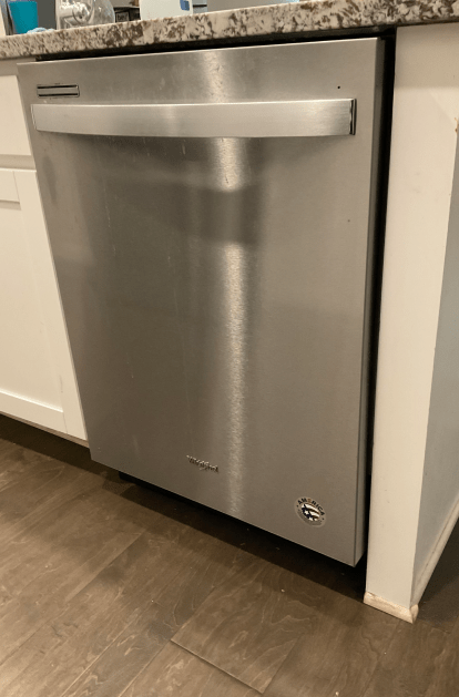 Stainless steel Whirlpool dishwasher installed in a kitchen, mounted between white cabinets.