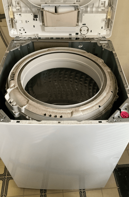 Open top-loading washing machine interior. Gray drum surrounded by white frame, lid open.