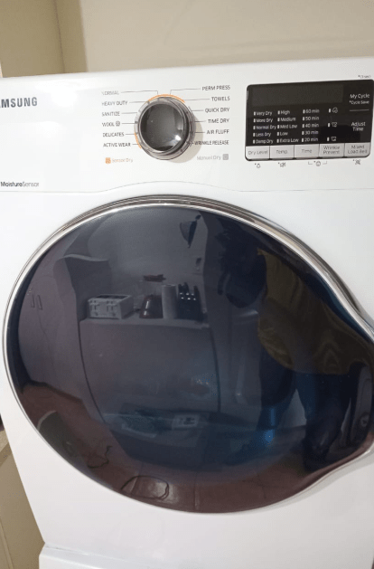 White Samsung washing machine with dark, reflective door. Control panel with dial and digital display.