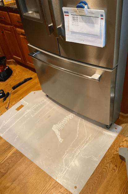 Stainless steel refrigerator on protective mat in a kitchen with wooden floor.