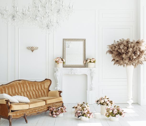 Elegant white room with gold sofa, fireplace, and flowers; large chandelier.