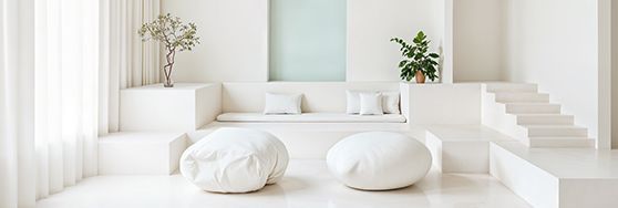 A minimalist white living room with soft seating, built-in bench, stairs, and plants.