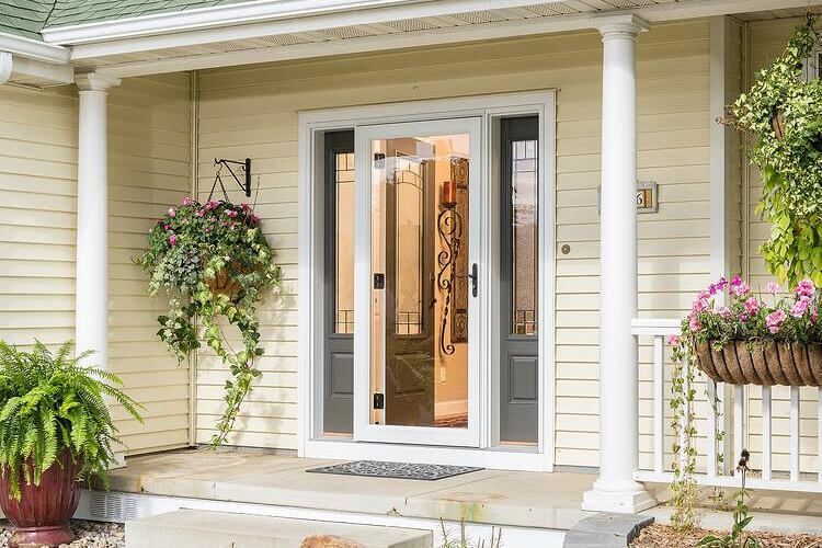 Beige house entrance with white trim, screen door, and hanging flower baskets.