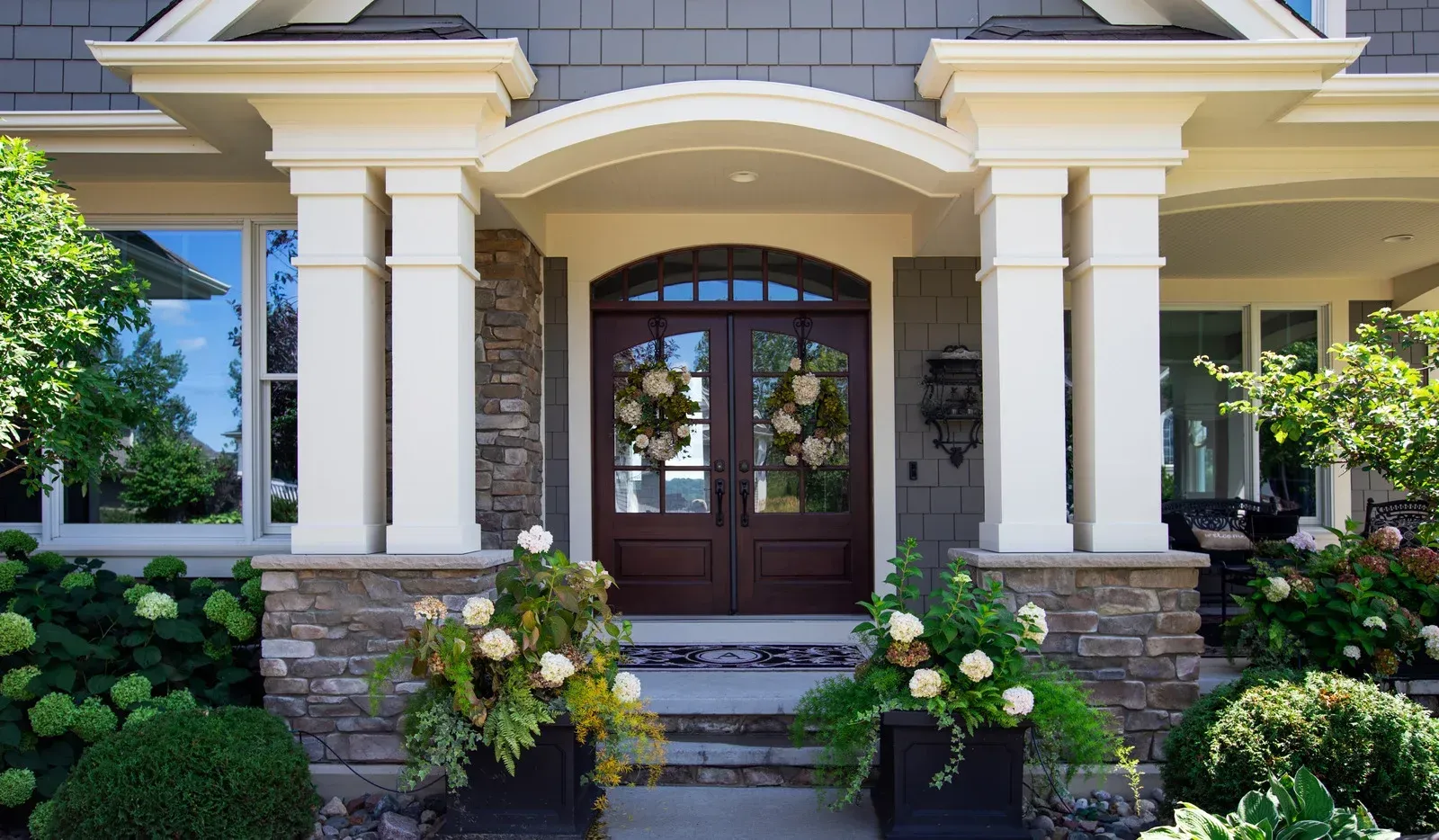 Front entrance with brown double doors, stone accents, white columns, and flower boxes.