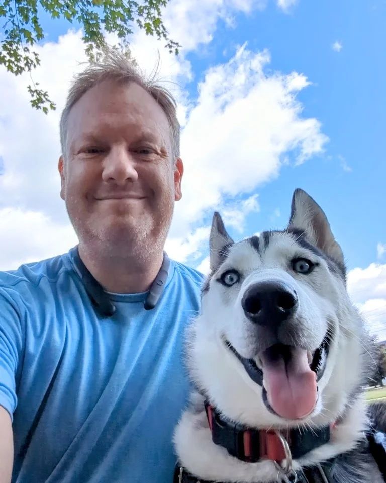 A man is taking a selfie with his husky dog.
