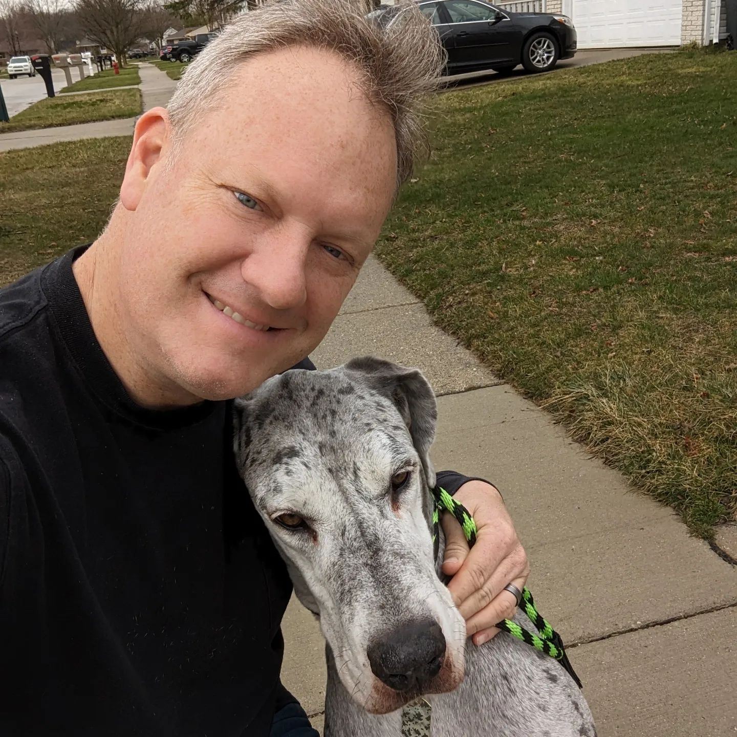 A man is posing for a picture with his dog on the sidewalk