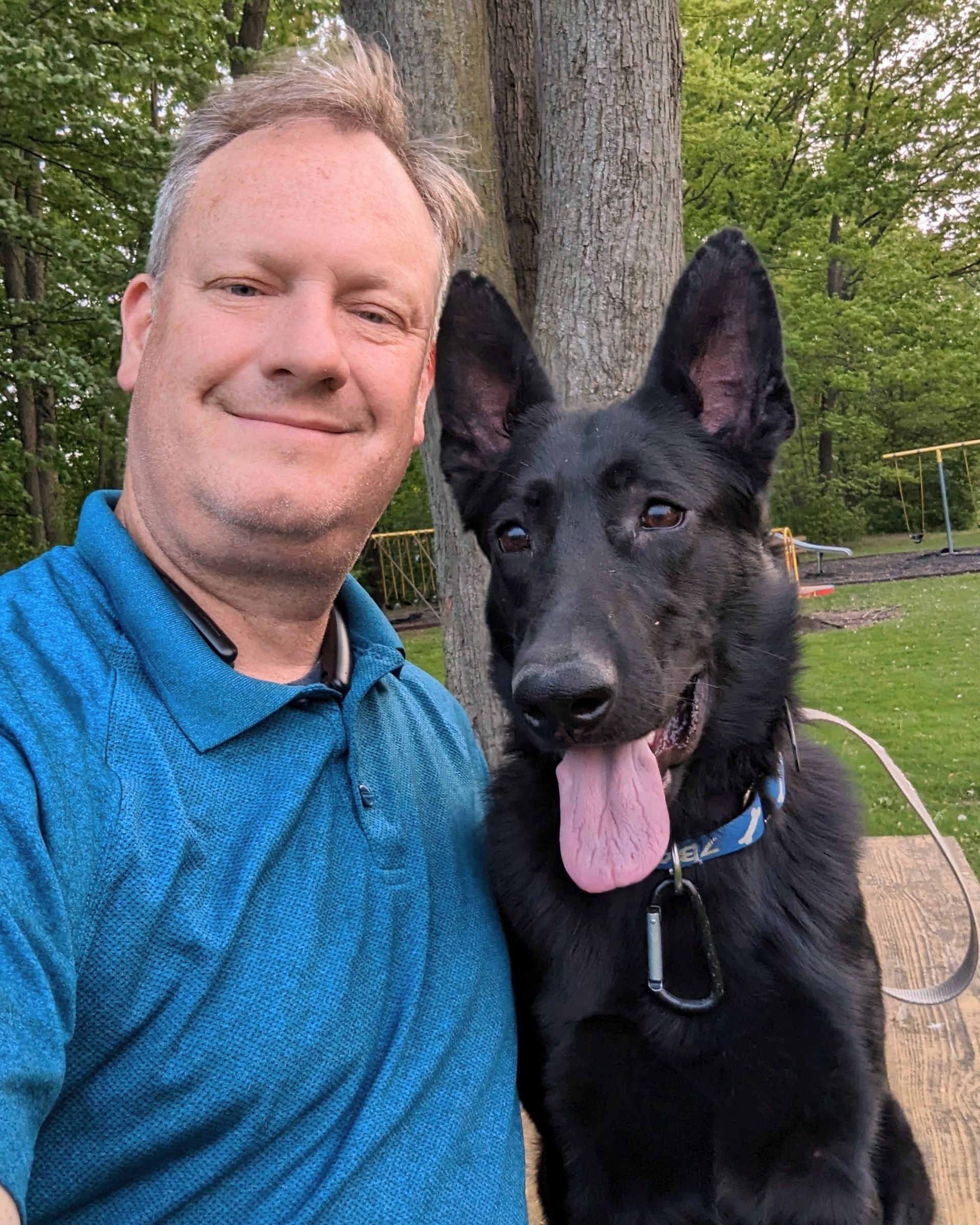 A man in a blue shirt is standing next to a black dog