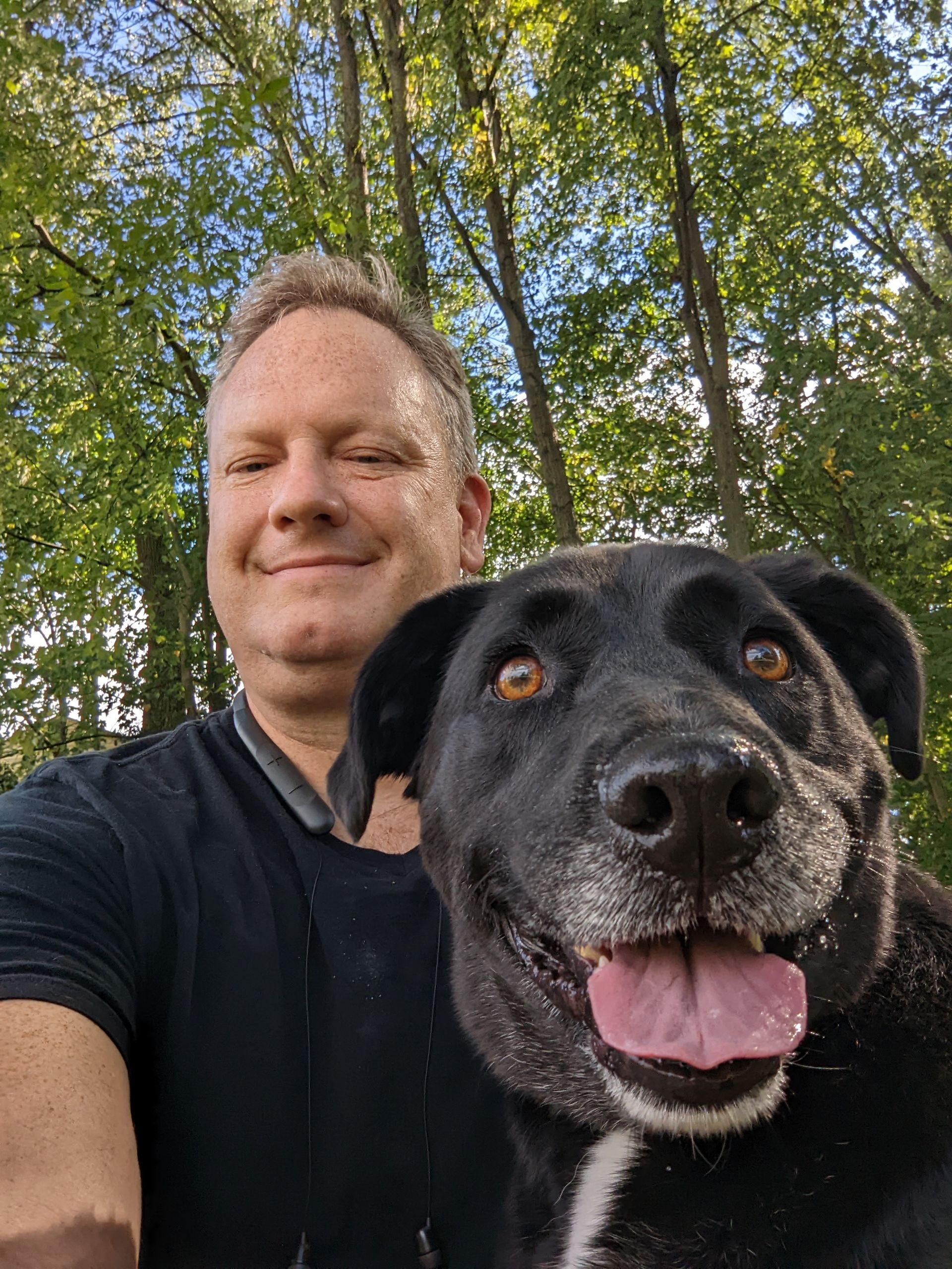 A man is taking a selfie with his black dog