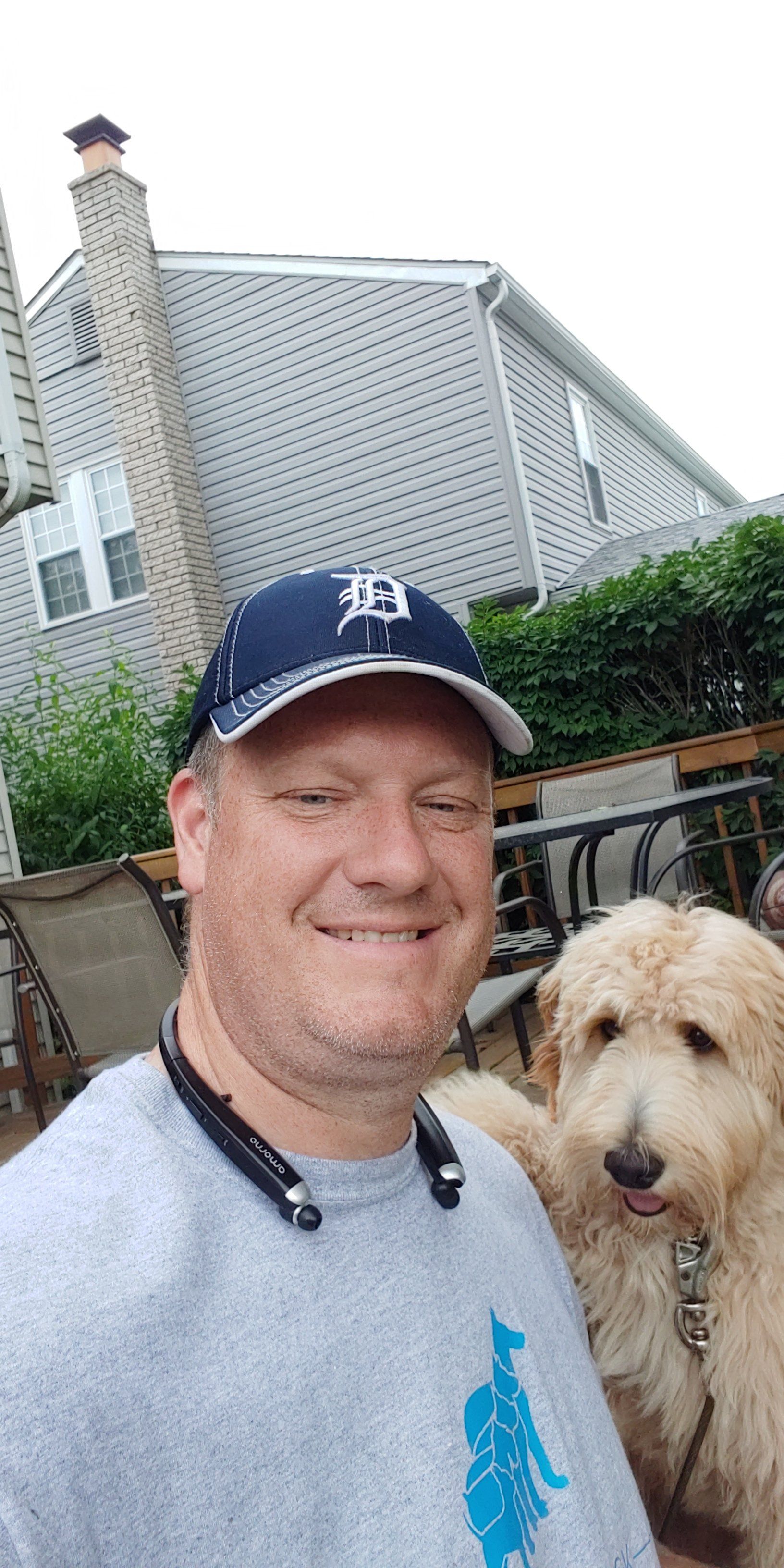 A man is taking a selfie with his dog in front of a house.