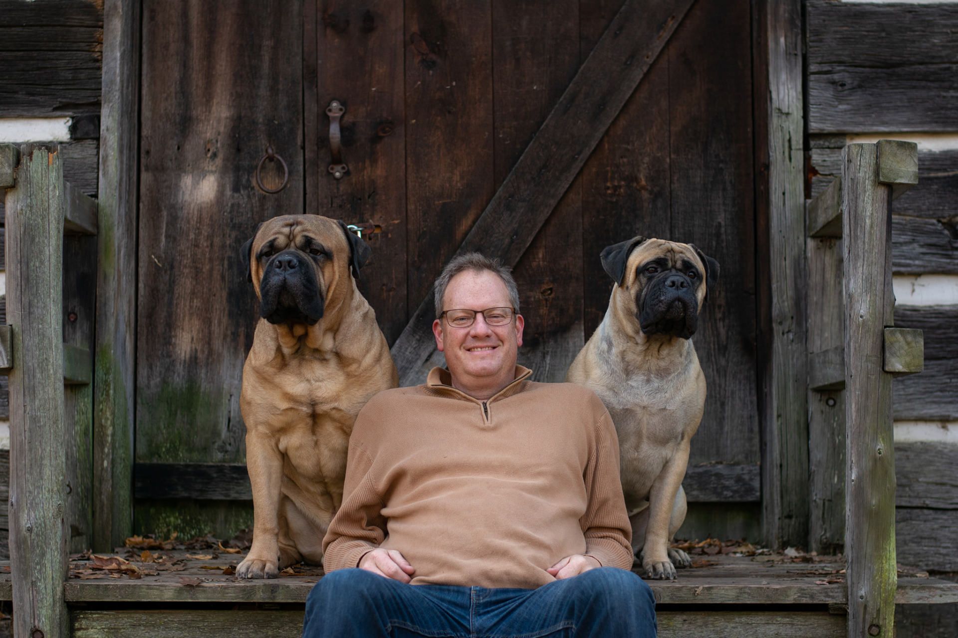 A dog trainer in Canton MI sits on a porch with two dogs