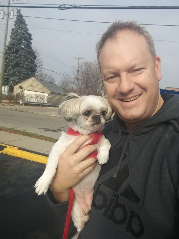 A man in a sweatshirt holds a small white dog while training it