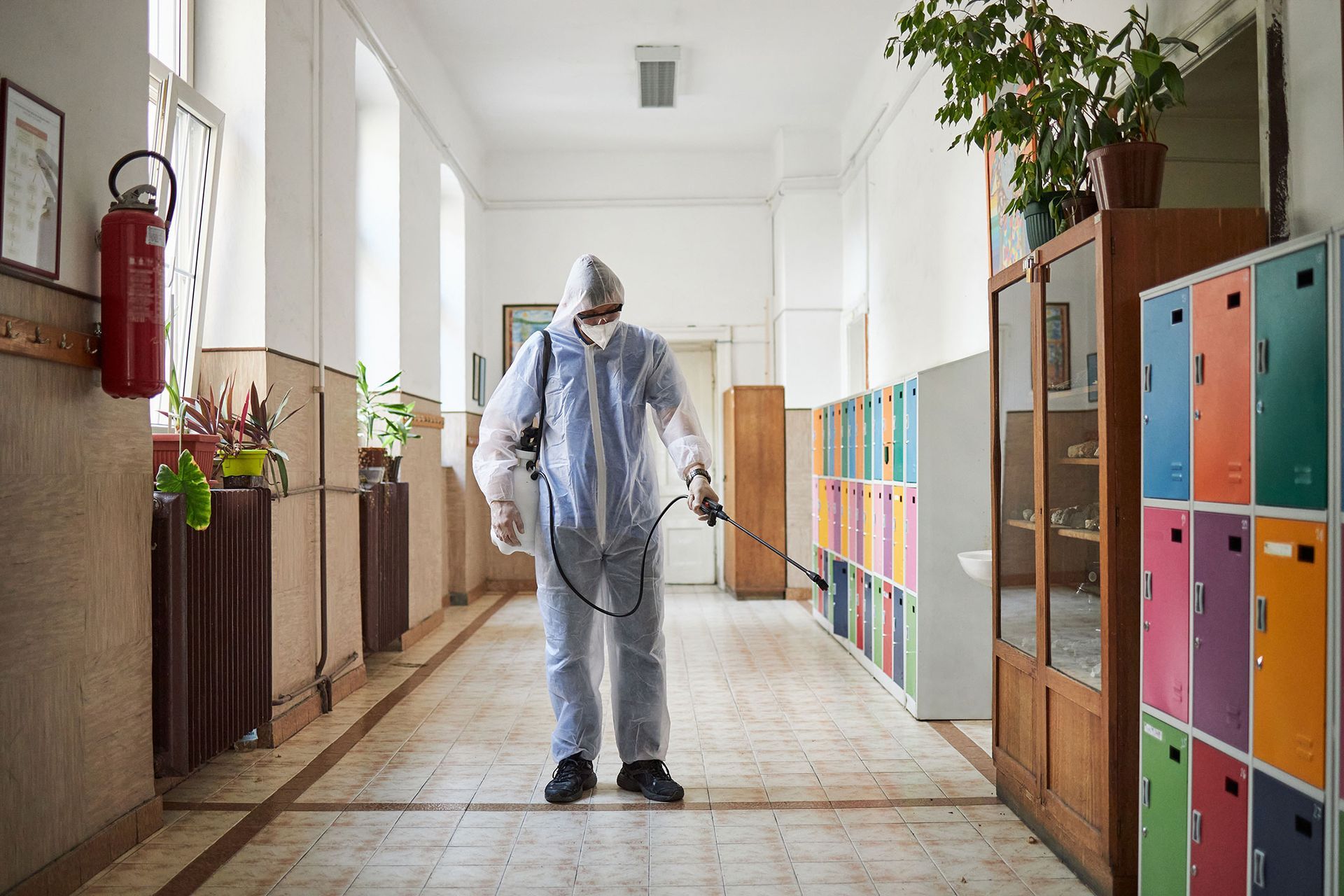 A man in a protective suit is disinfecting a hallway in a school.