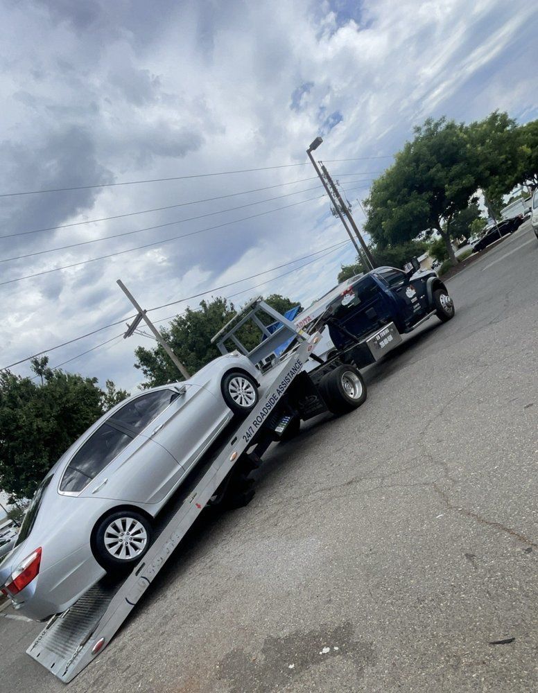 Silver car being towed up a ramp by a flatbed tow truck on a cloudy day.