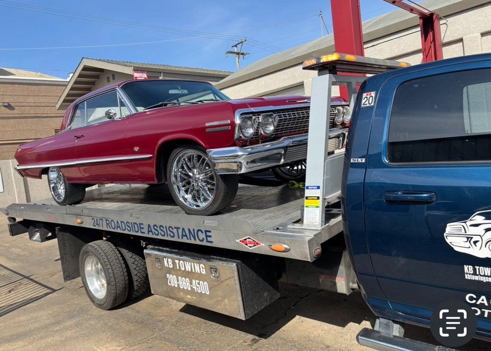 A classic burgundy car on a flatbed tow truck.