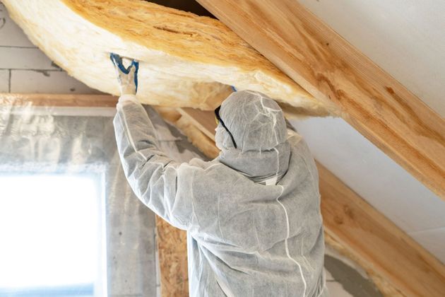 Interior construction site with yellow insulation between wooden beams; ladder leans against window.