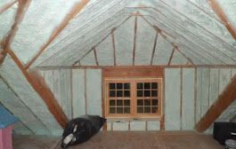 Person in protective suit spraying insulation foam on a ceiling.