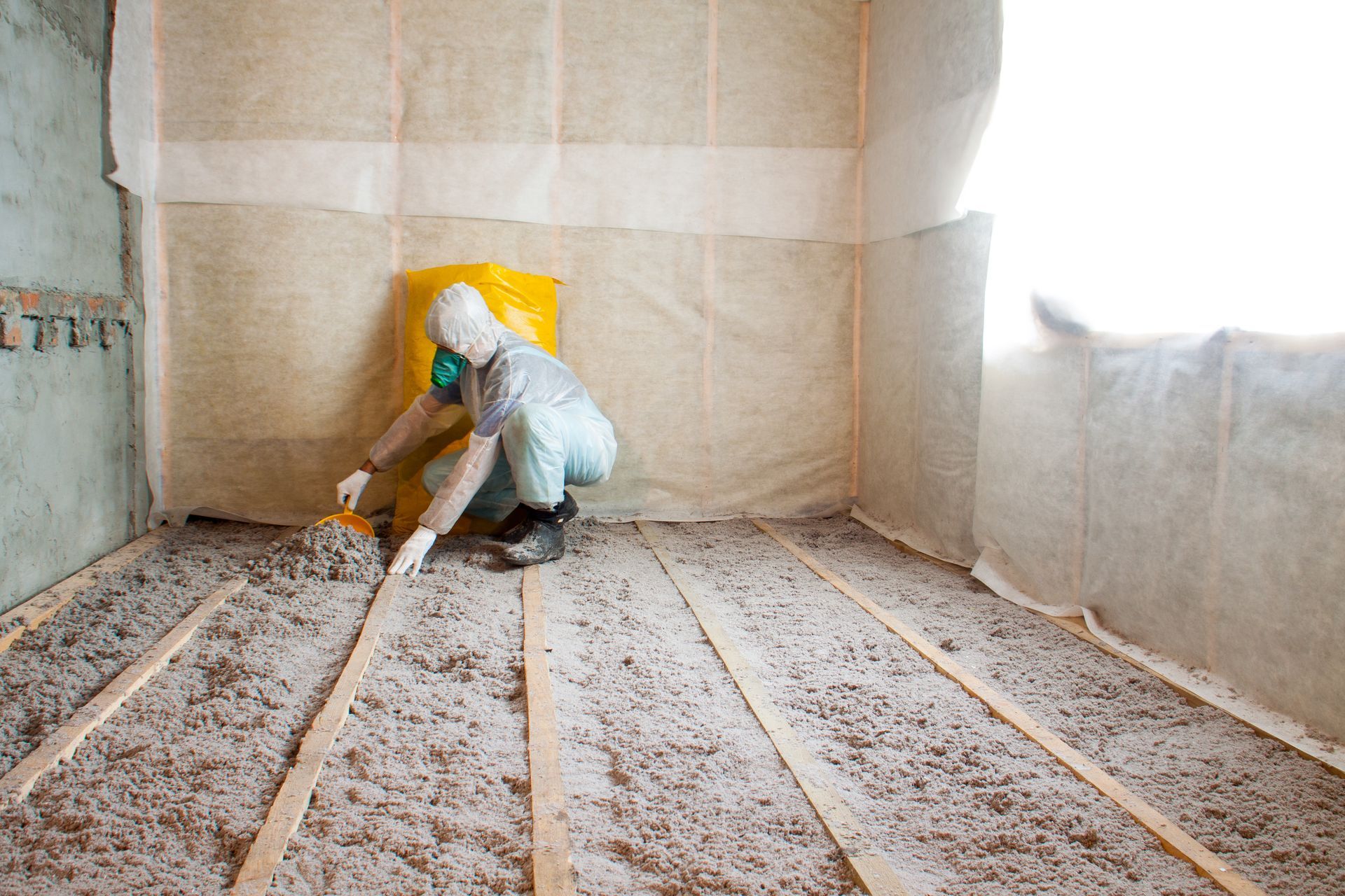 Person spreading insulation in a room, wearing protective gear. Person spreading insulation in a room, wearing protective gear.