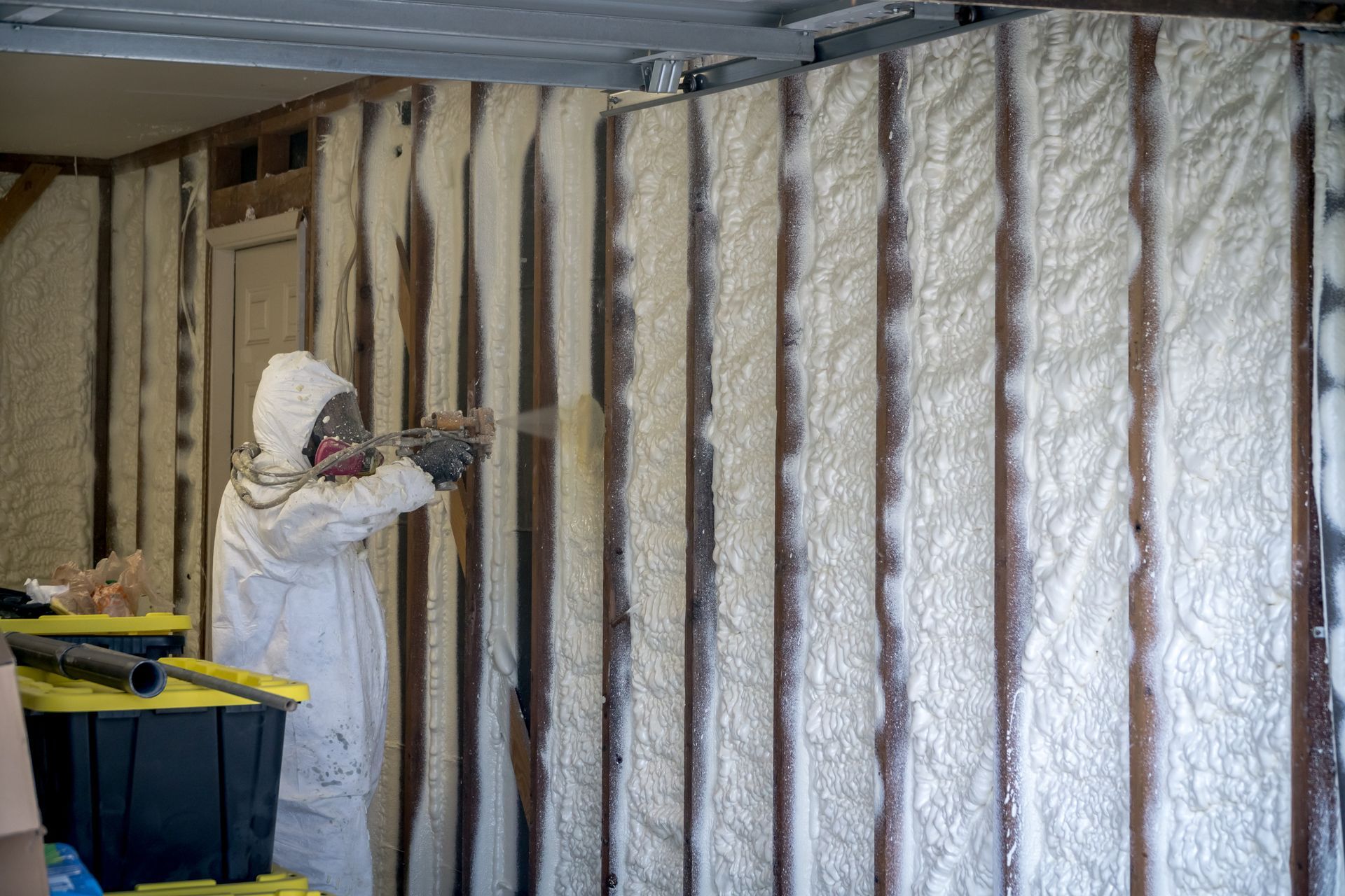 Person in protective suit spraying insulation foam on a wall. Person in protective suit spraying insulation foam on a wall.