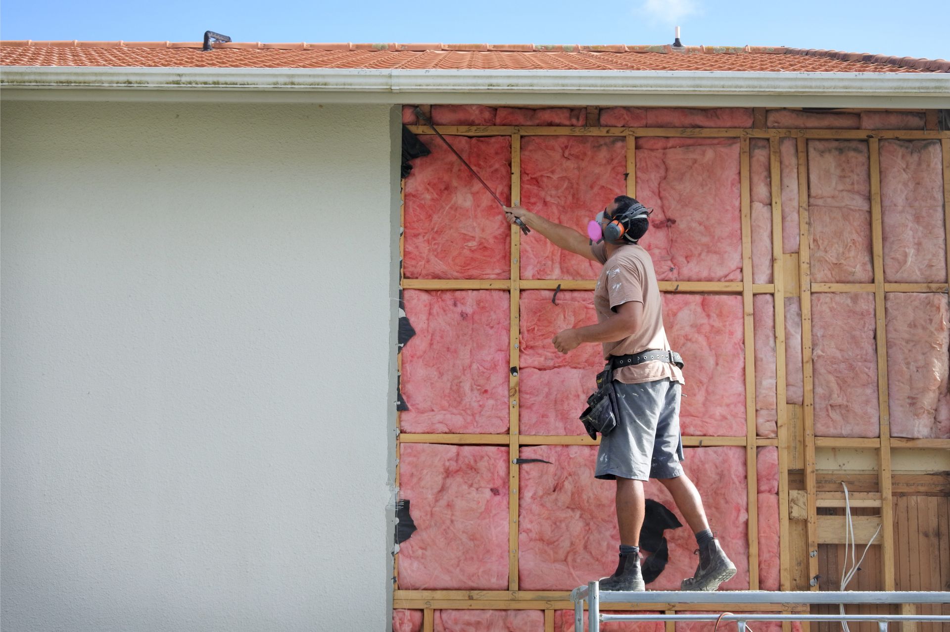 Construction worker on scaffolding, removing siding from a building, revealing insulation. Construction worker on scaffolding, removing siding from a building, revealing insulation.