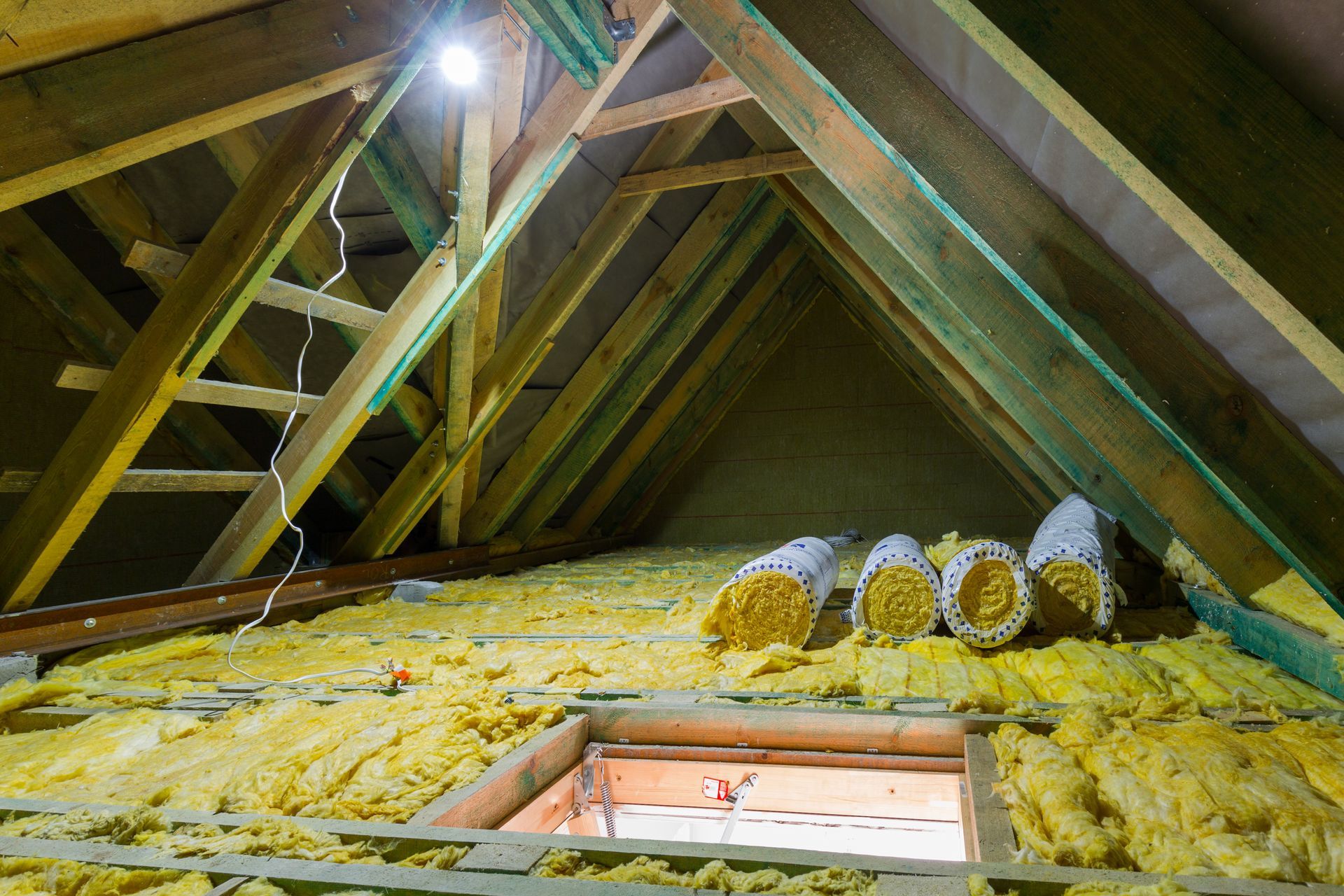 Attic interior with yellow insulation, wooden rafters, a hatch, and a ladder. Attic interior with yellow insulation, wooden rafters, a hatch, and a ladder.
