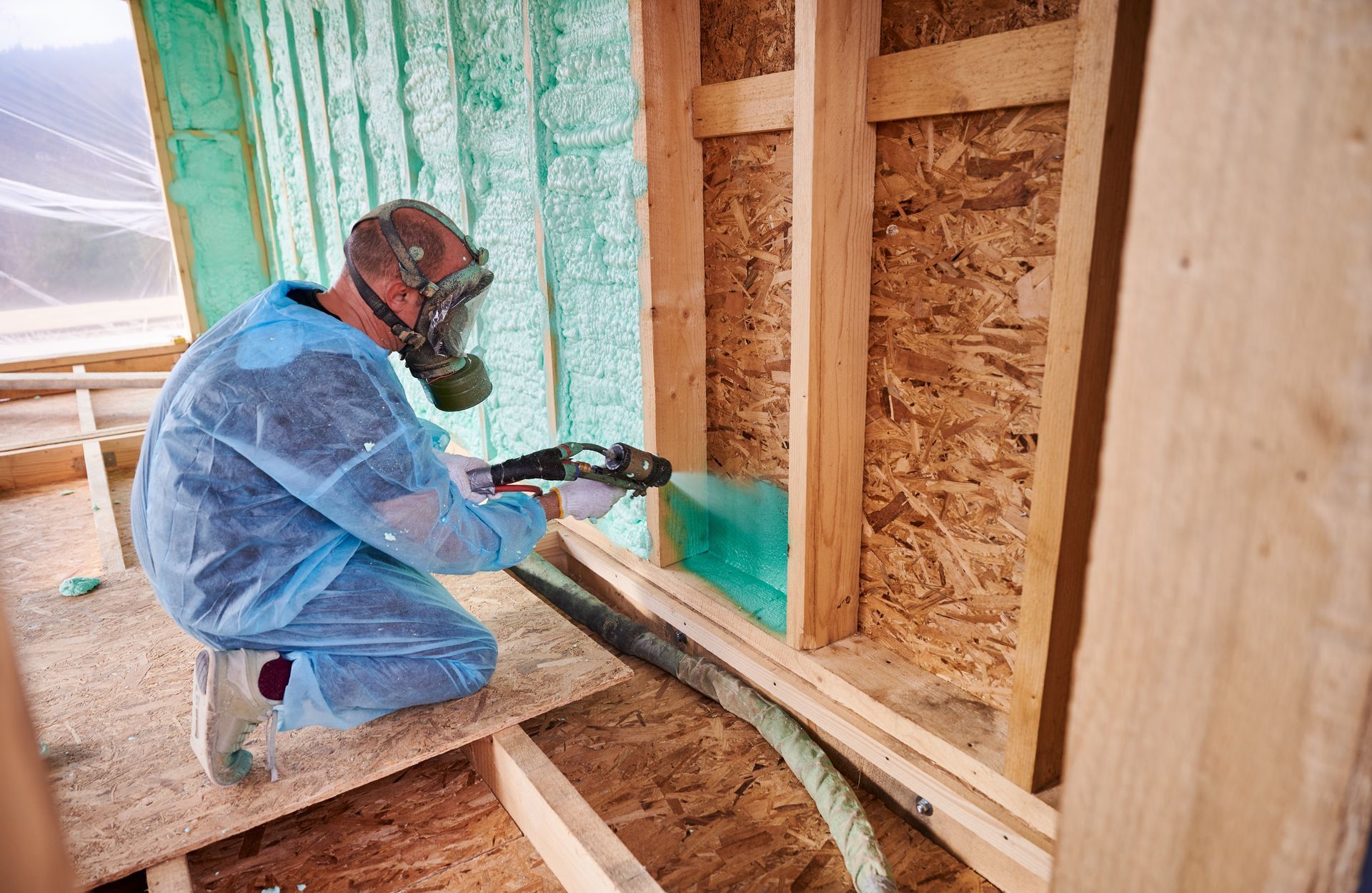 Person in protective gear sprays insulation into a wooden frame during construction. Person in protective gear sprays insulation into a wooden frame during construction.